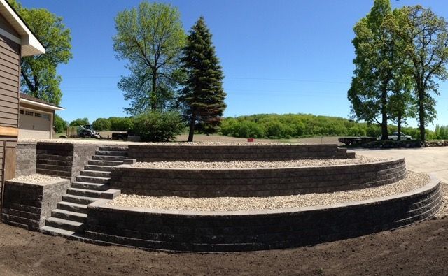 Stone terraced steps and a raised patio beside a building, with trees and blue sky in the background