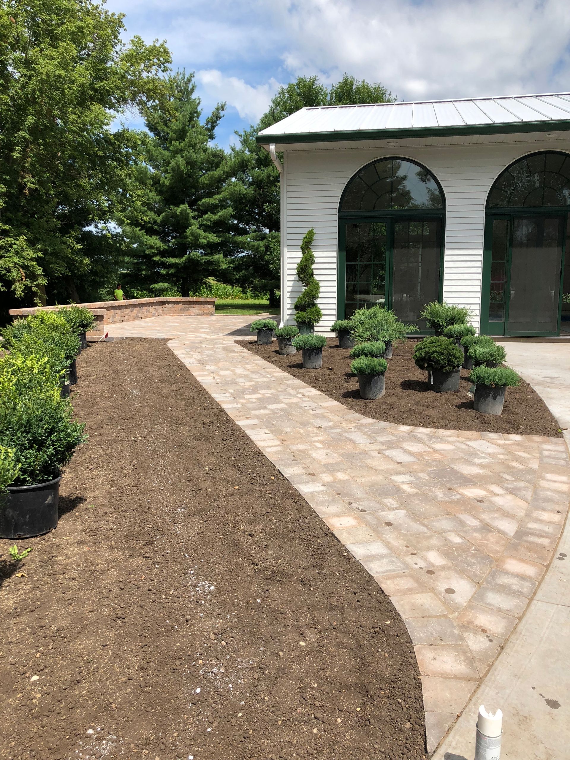 Curved stone walkway beside a white building with arched windows, bordered by newly planted beds and greenery