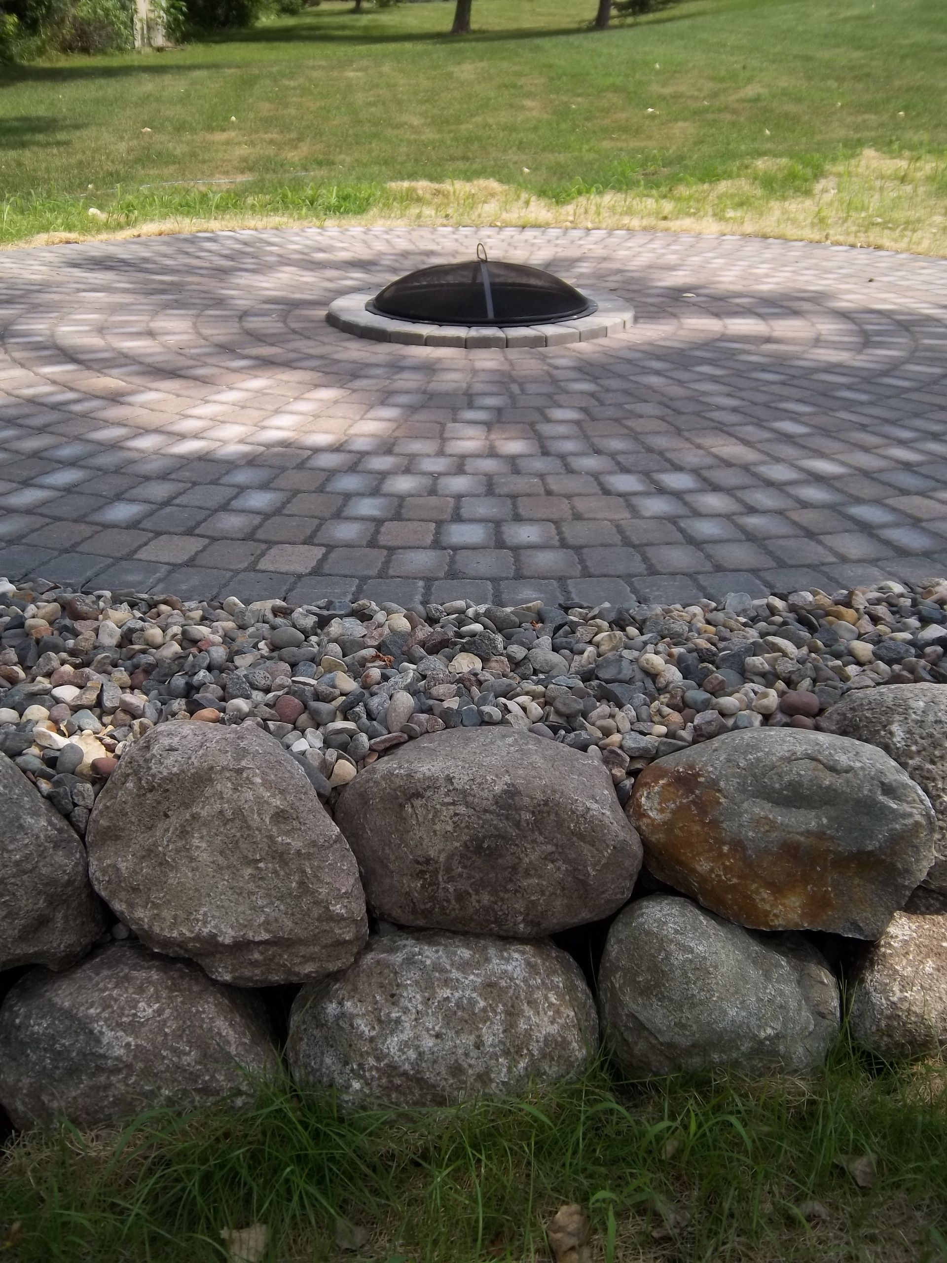 Stone-ring fire pit in a grassy park, with a low rock border in front