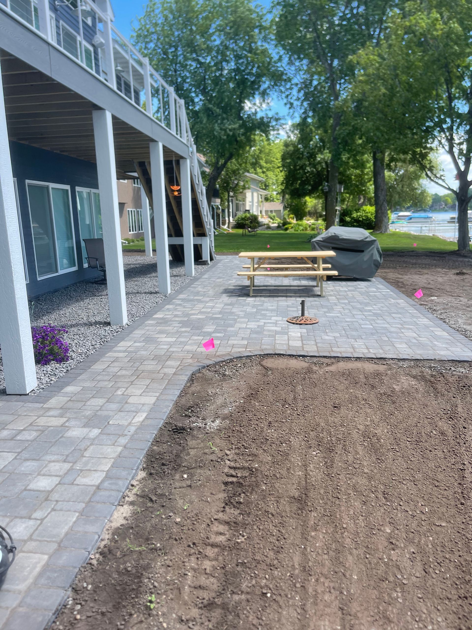 Backyard patio beside a house with pavers, mulch, and a lake view through trees