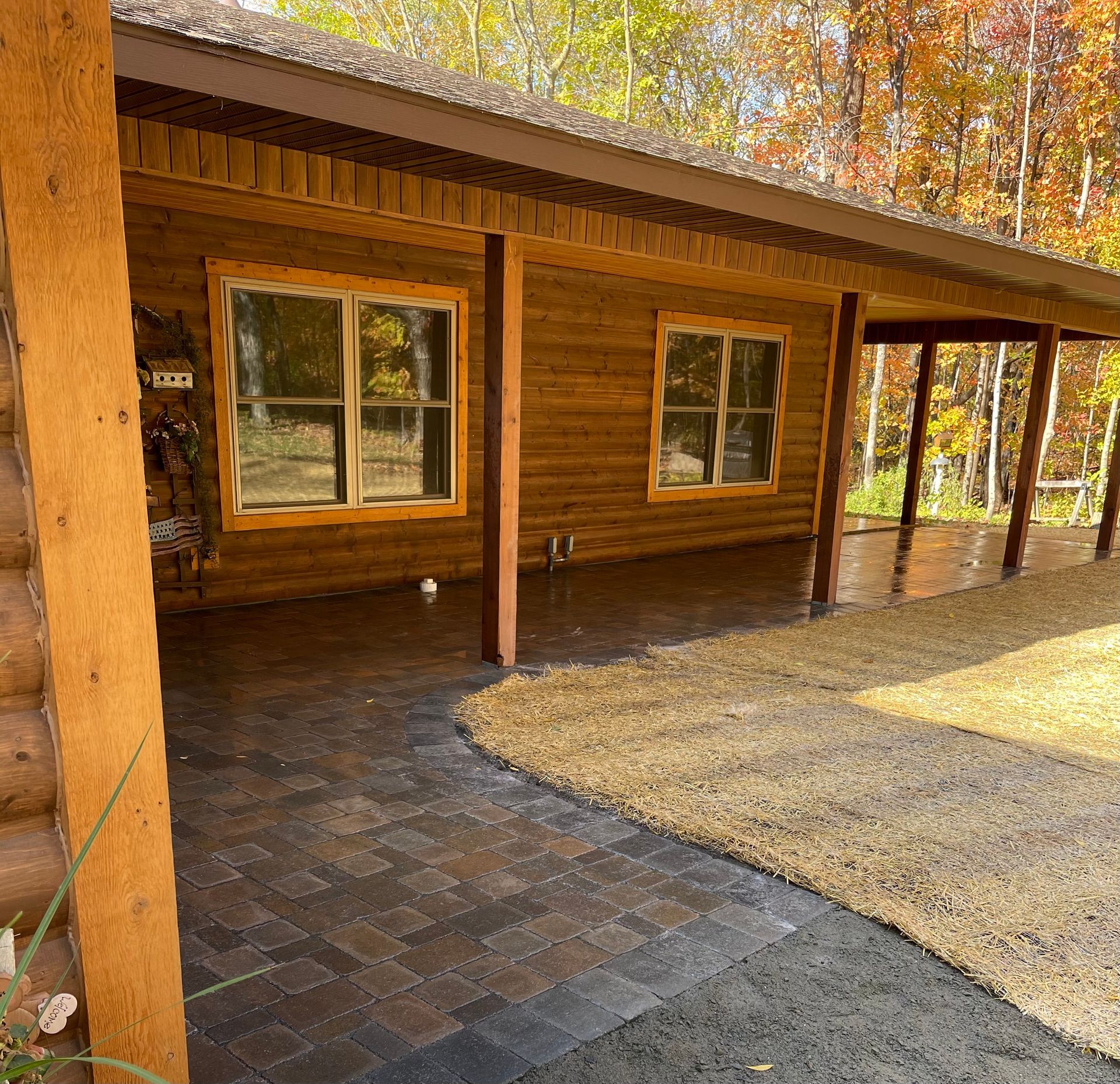 Wooden cabin porch with windows, brick pavers, and autumn trees in the background