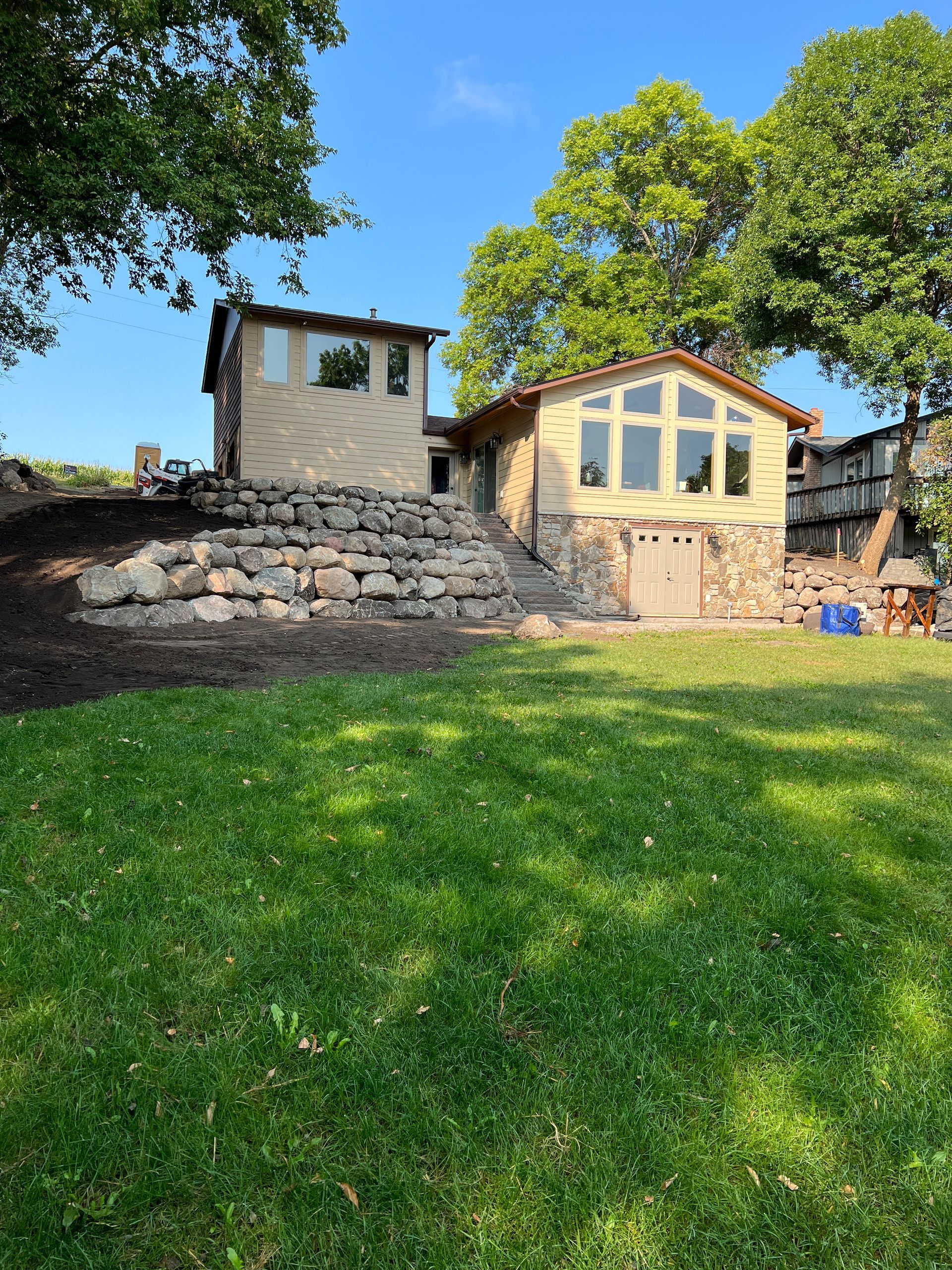 Stone terrace with a small cream house and green lawn under bright blue sky