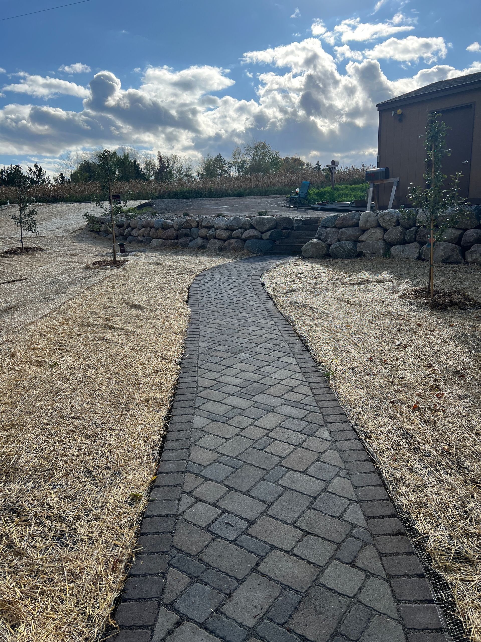 Stone path through a gravel yard toward a low wall and building under a partly cloudy sky