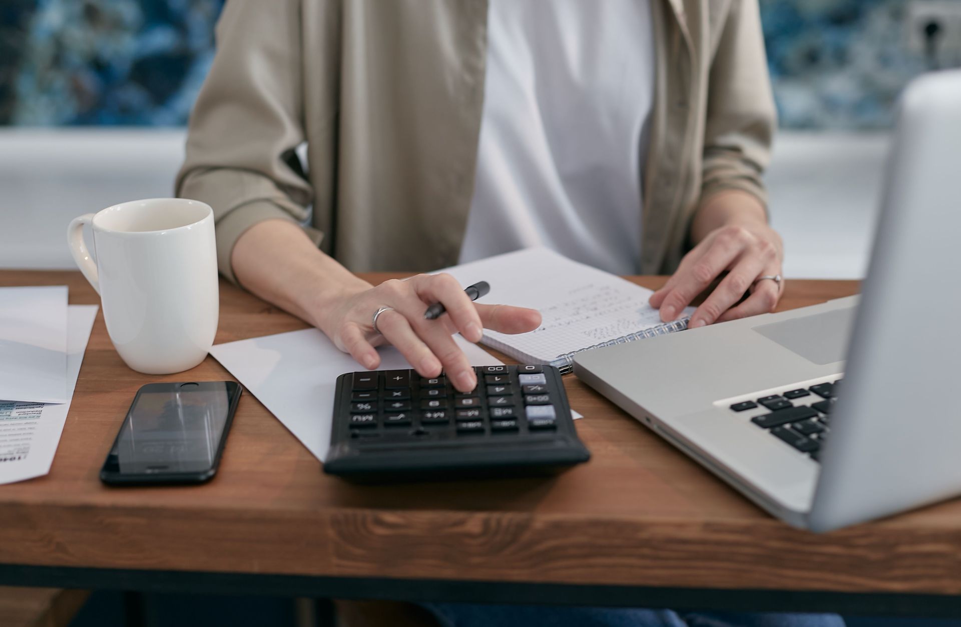 Person reviewing financial calculations with a calculator, notebook and laptop.