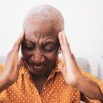 Person holding their temples with eyes closed, looking stressed against a white background