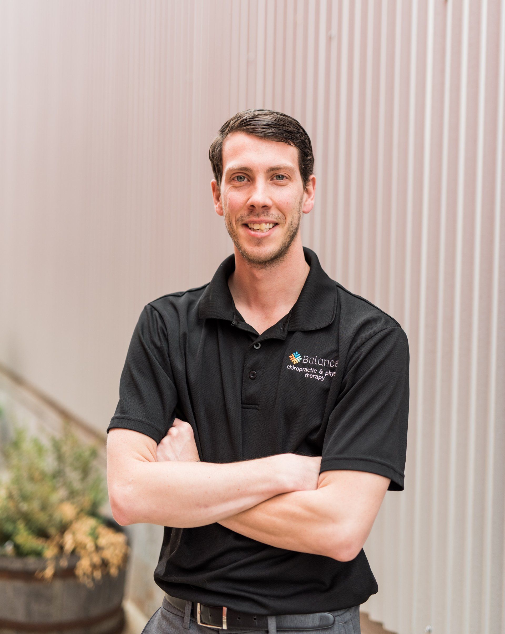 Man in a black polo shirt standing with arms crossed in front of a corrugated metal wall