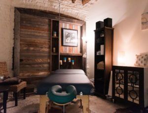 Cozy bedroom with wood-paneled wall, bed, teal chair, and warm lighting