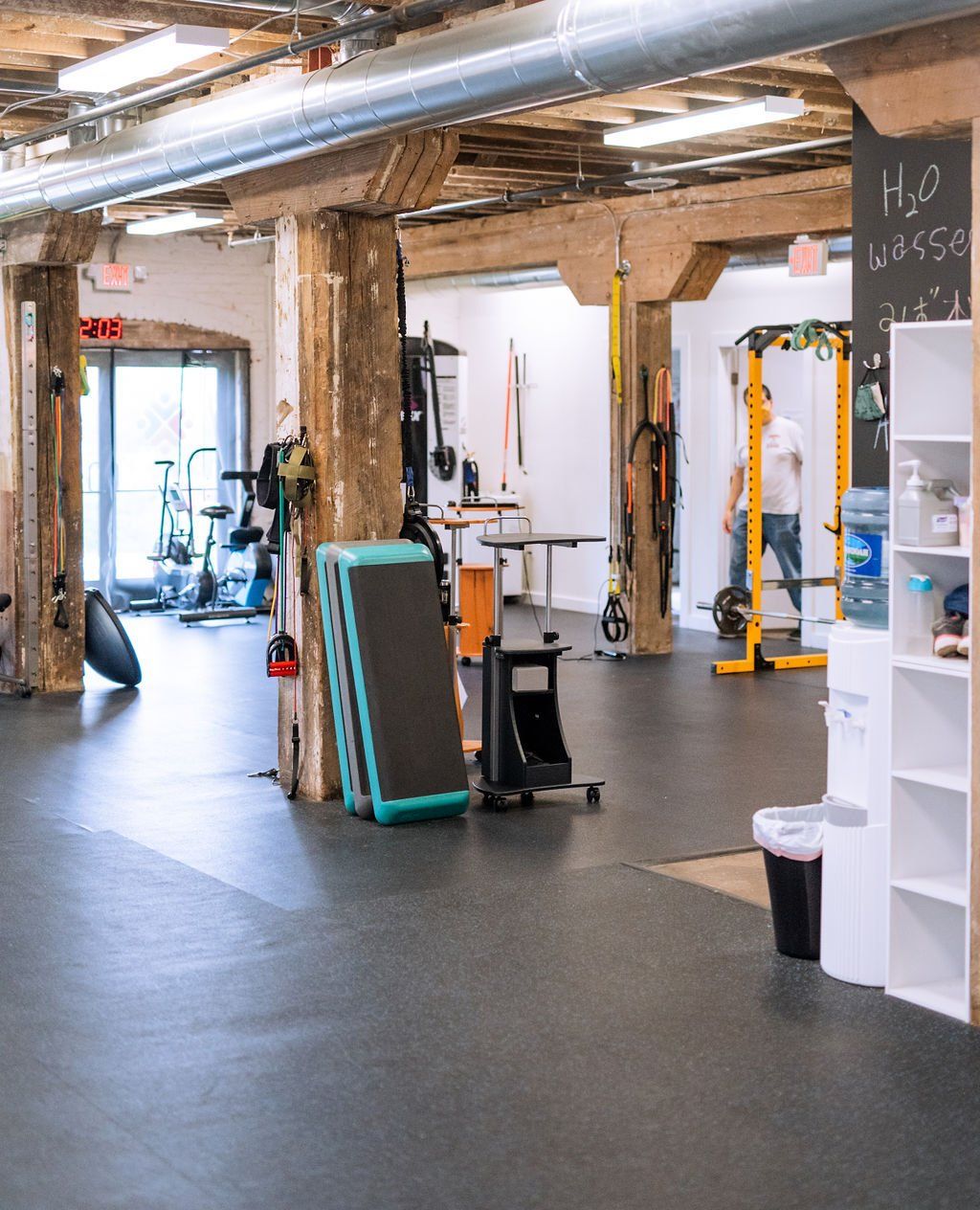 Bright gym interior with exercise equipment, wooden beams, and a dark floor
