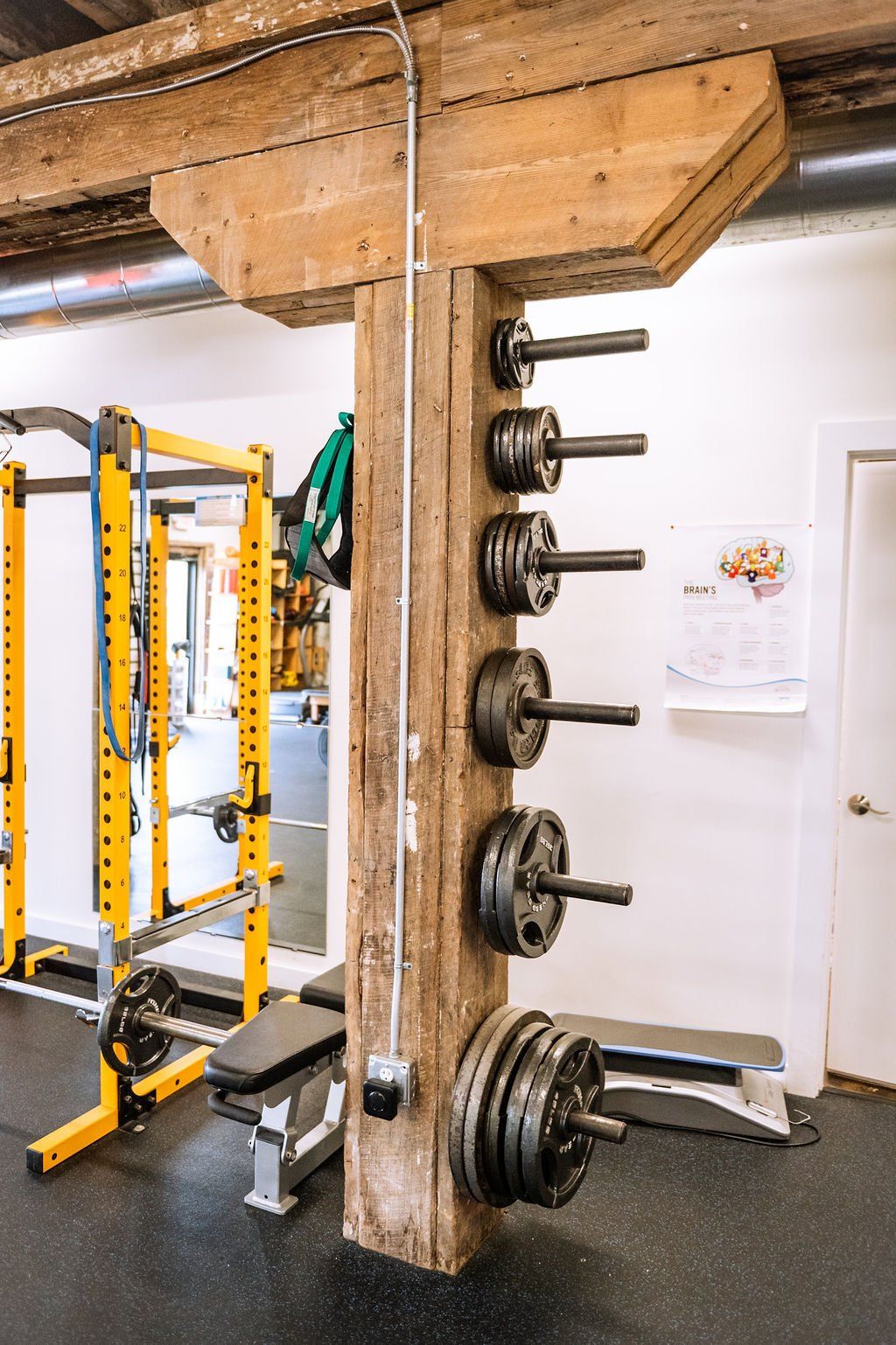 Rustic gym corner with weight plates mounted on a wooden post and yellow exercise equipment nearby