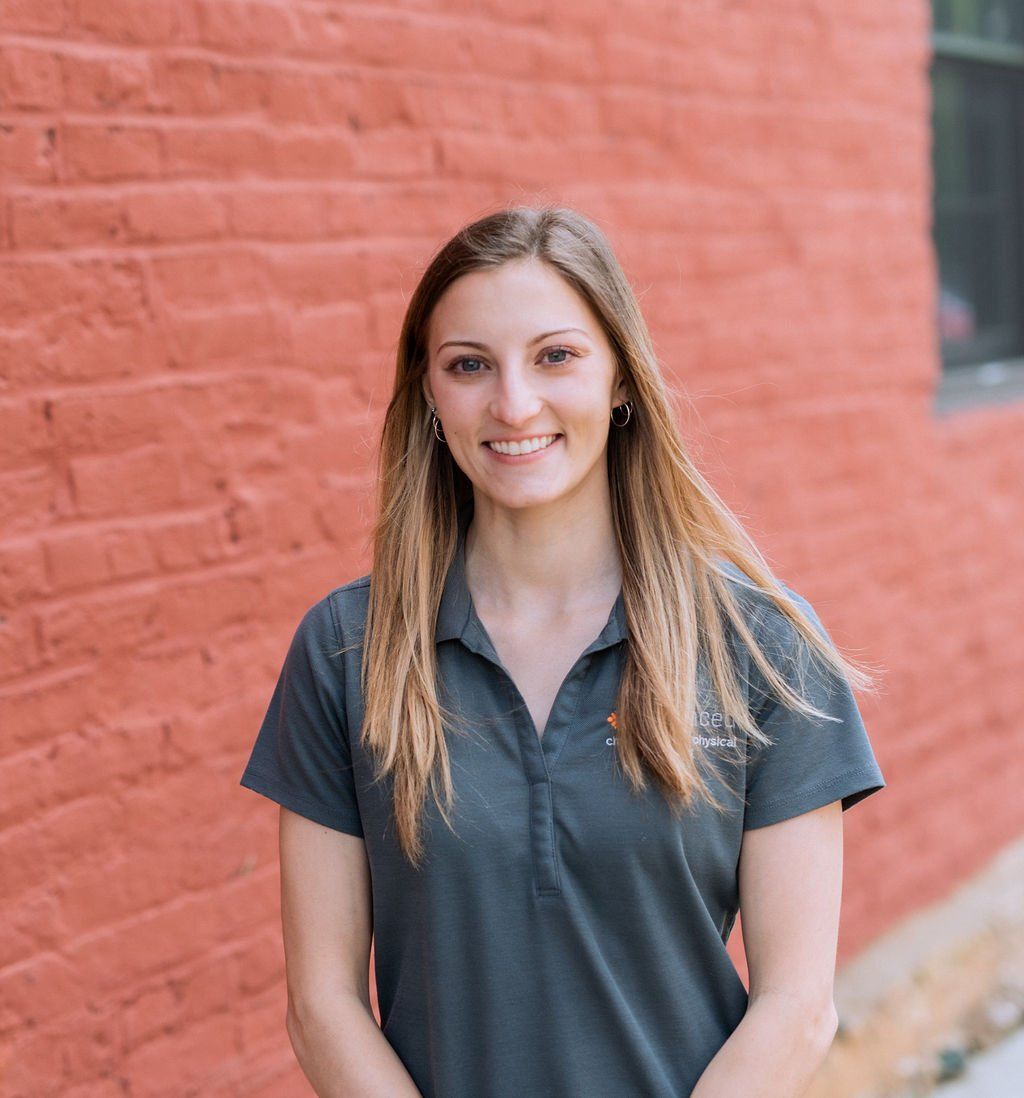 Smiling woman in a dark gray shirt standing against a red brick wall