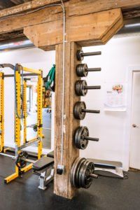 Weight plates and barbells mounted on a wooden beam in a gym storage area.