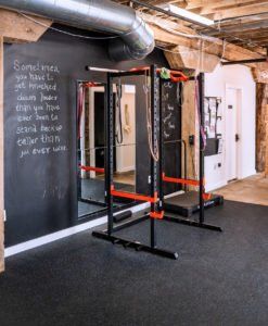 Gym with pull-up bars, black mats, chalkboard wall, and exposed ceiling beams.