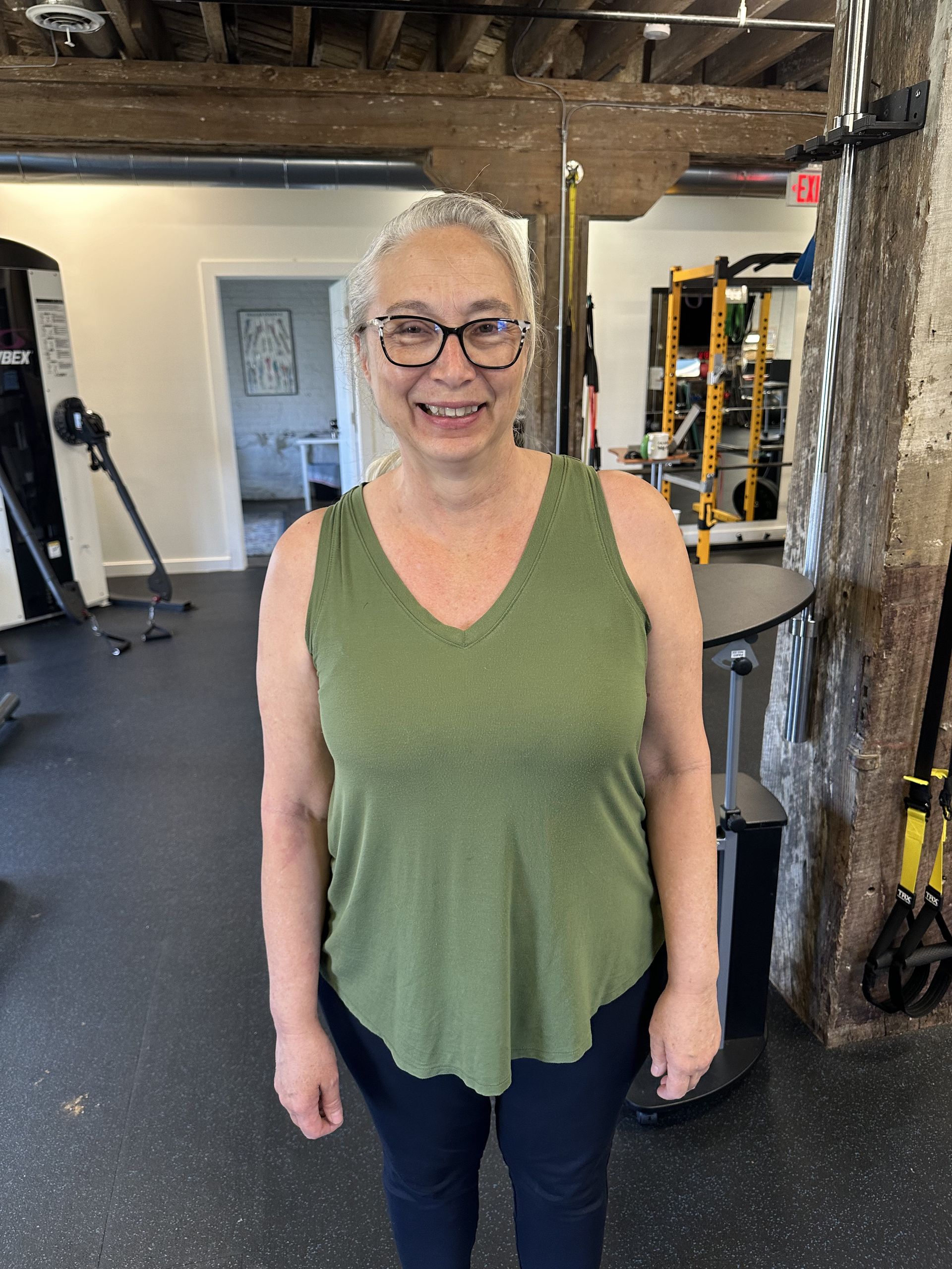 Smiling person in a green top and black pants standing in a gym.
