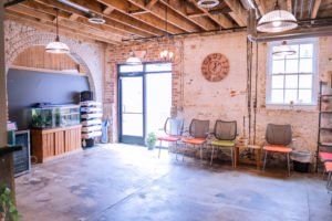 Rustic brick room with wood-beam ceiling, large TV, cabinet, and row of chairs by bright windows