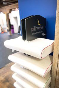 Stack of white pillows with a black “Pillowise” display sign on top.