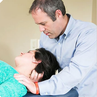 Man in blue shirt supporting a woman lying back, examining her neck in a clinical setting