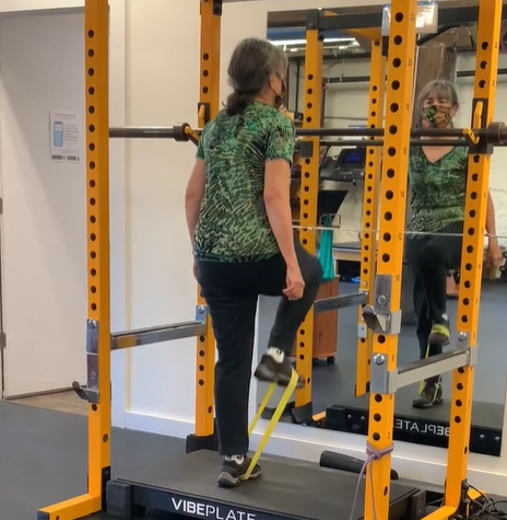 Woman using resistance bands on a gym machine in a mirrored fitness studio.