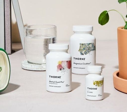 THORNE supplement bottles on a light tabletop beside a glass of water and a potted plant