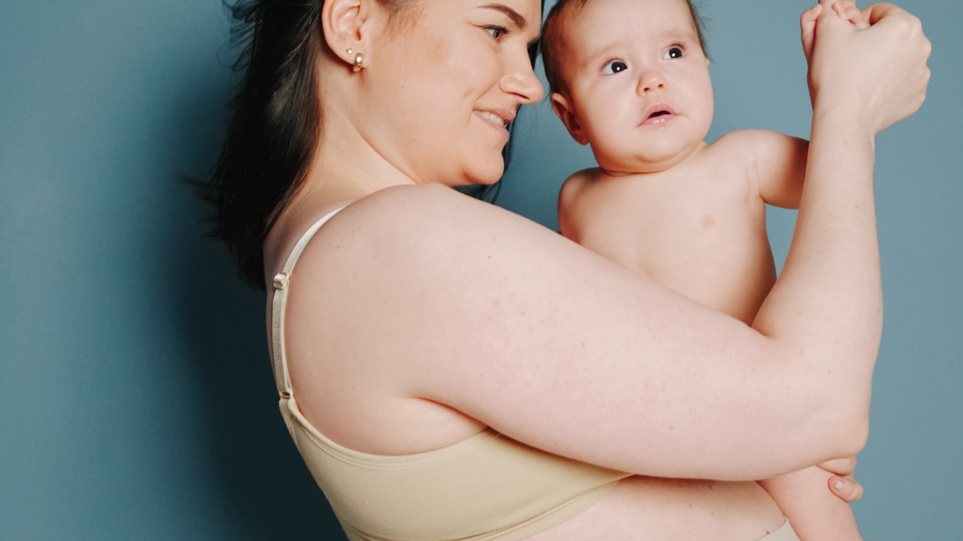 Woman holding a baby against a blue background, both looking to the side.