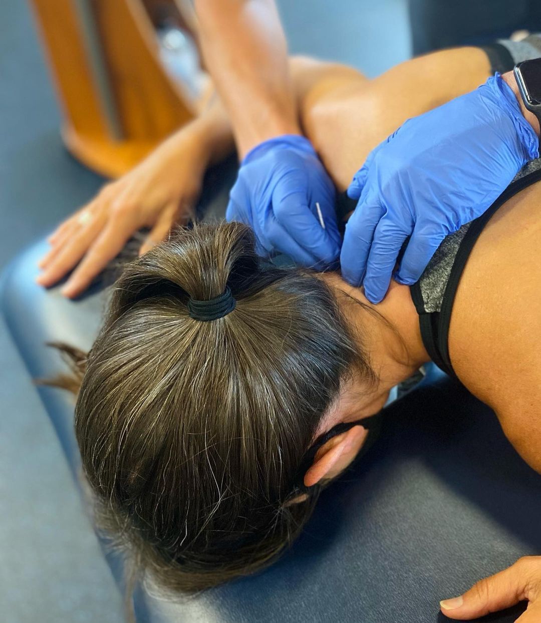 Gloved hands performing a neck massage on a person lying face down on a table