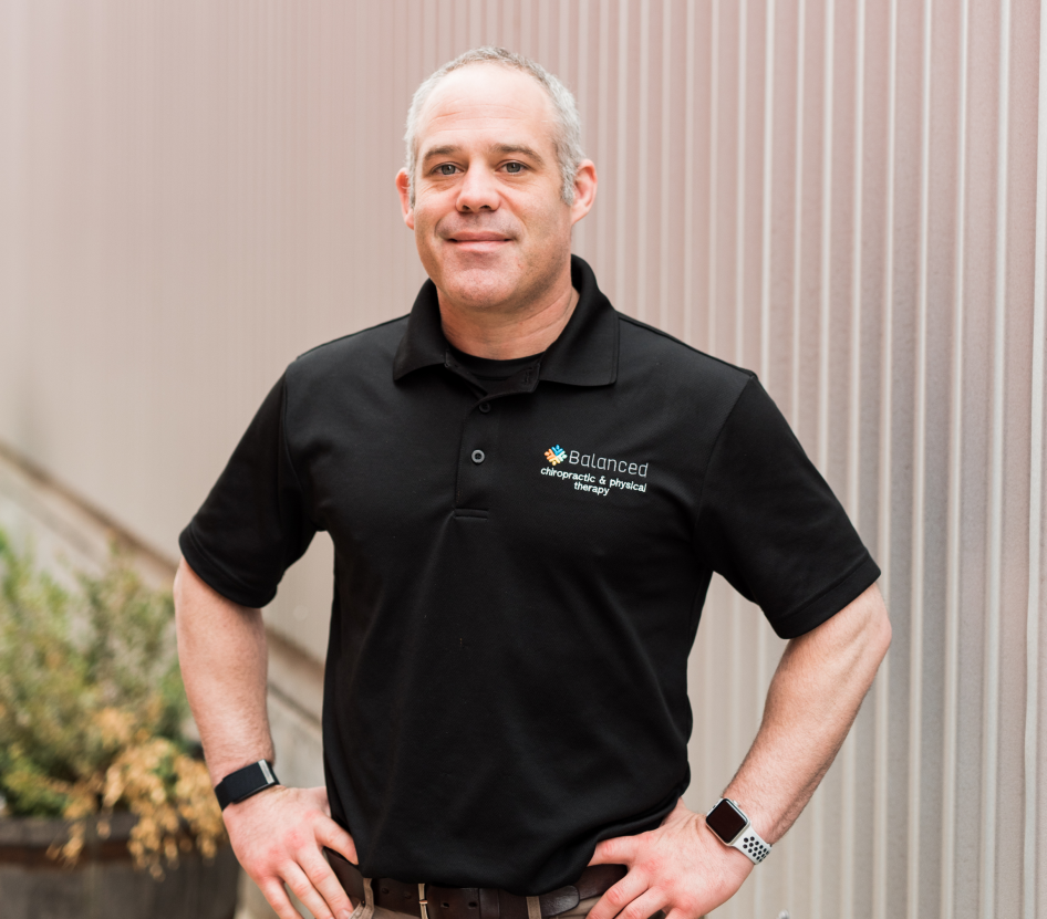 Man in black polo shirt standing with hands on hips against a striped wall