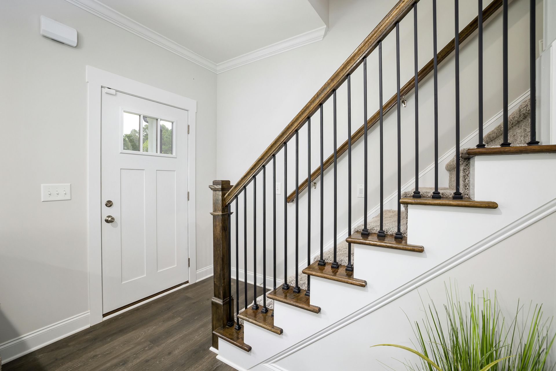 Bright entry hallway with a white front door, staircase with dark railing, and gray walls