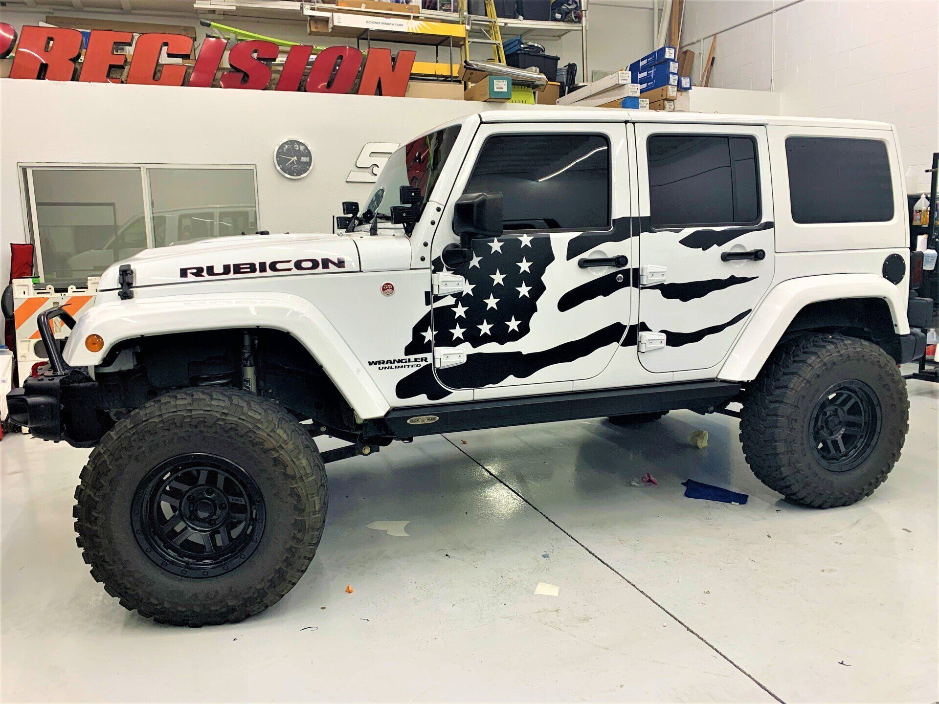 A white jeep with an american flag wrap on it is parked in a garage