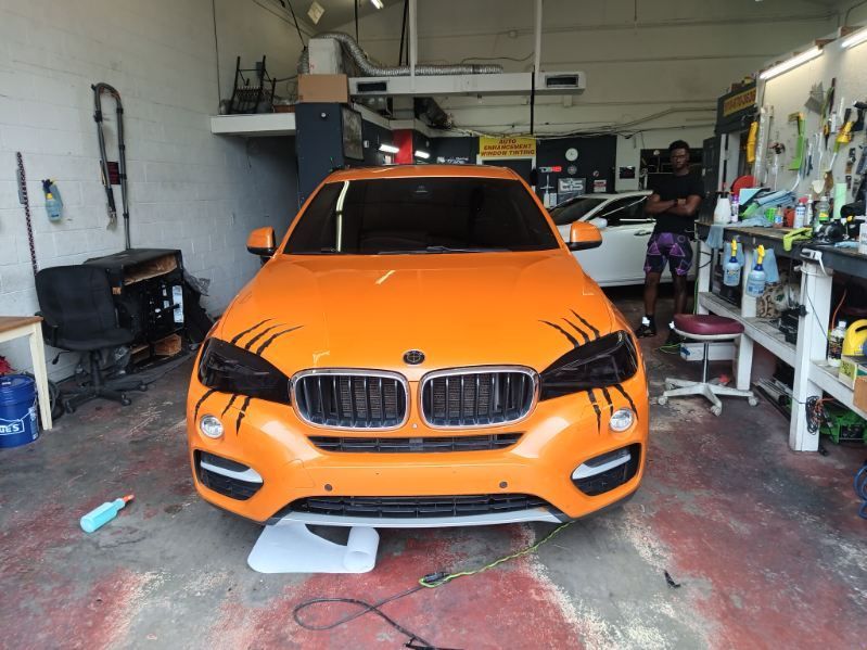 An orange bmw is sitting in a garage with a man standing behind it.