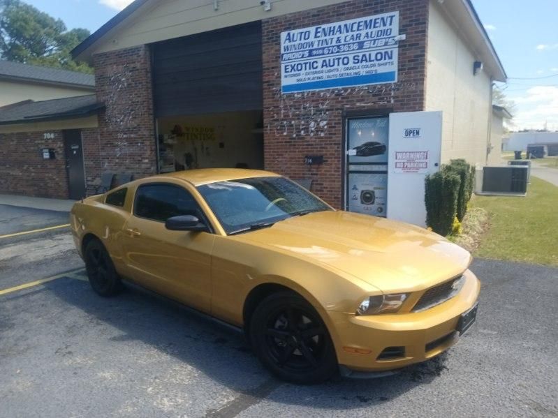 A yellow mustang is parked in front of a brick building.