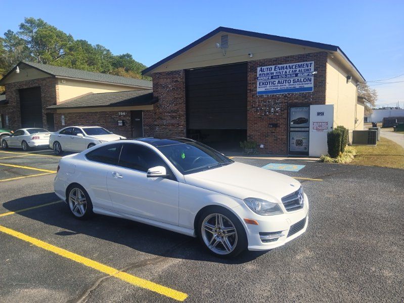 A white mercedes benz c class coupe is parked in a parking lot in front of a building.