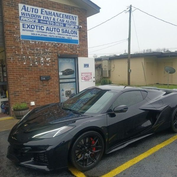 A black sports car is parked in a parking lot in front of a brick building.