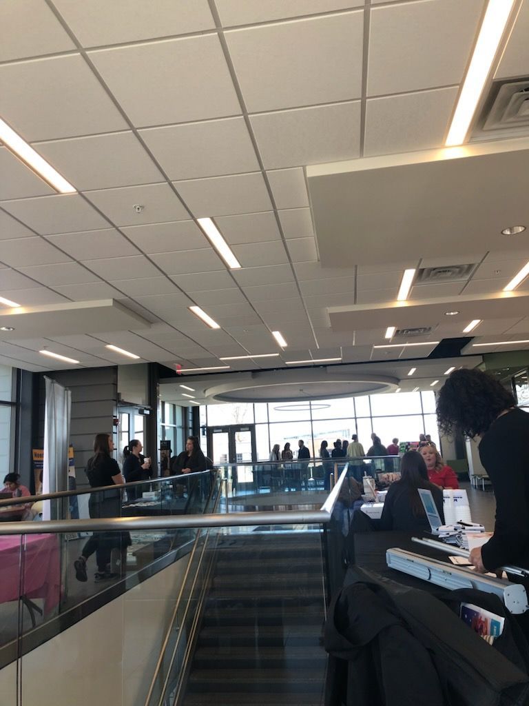 Airport terminal waiting area with travelers, escalators, and bright overhead lights