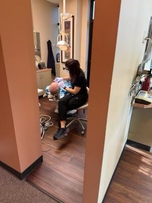 Dentist treating a patient in a small exam room, seen through a doorway.