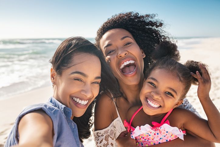 Three smiling friends taking a selfie at the beach with ocean waves behind them