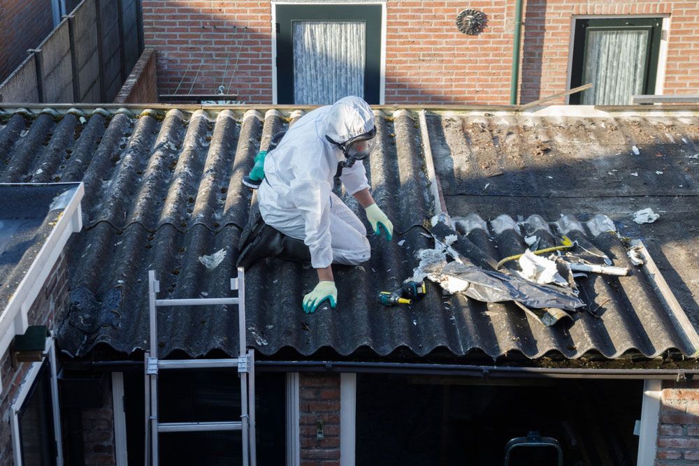 A Man in a Protective Suit is Working on the Roof of a House Removing Asbestos — Adzcom Civils in Portsmith, QLD