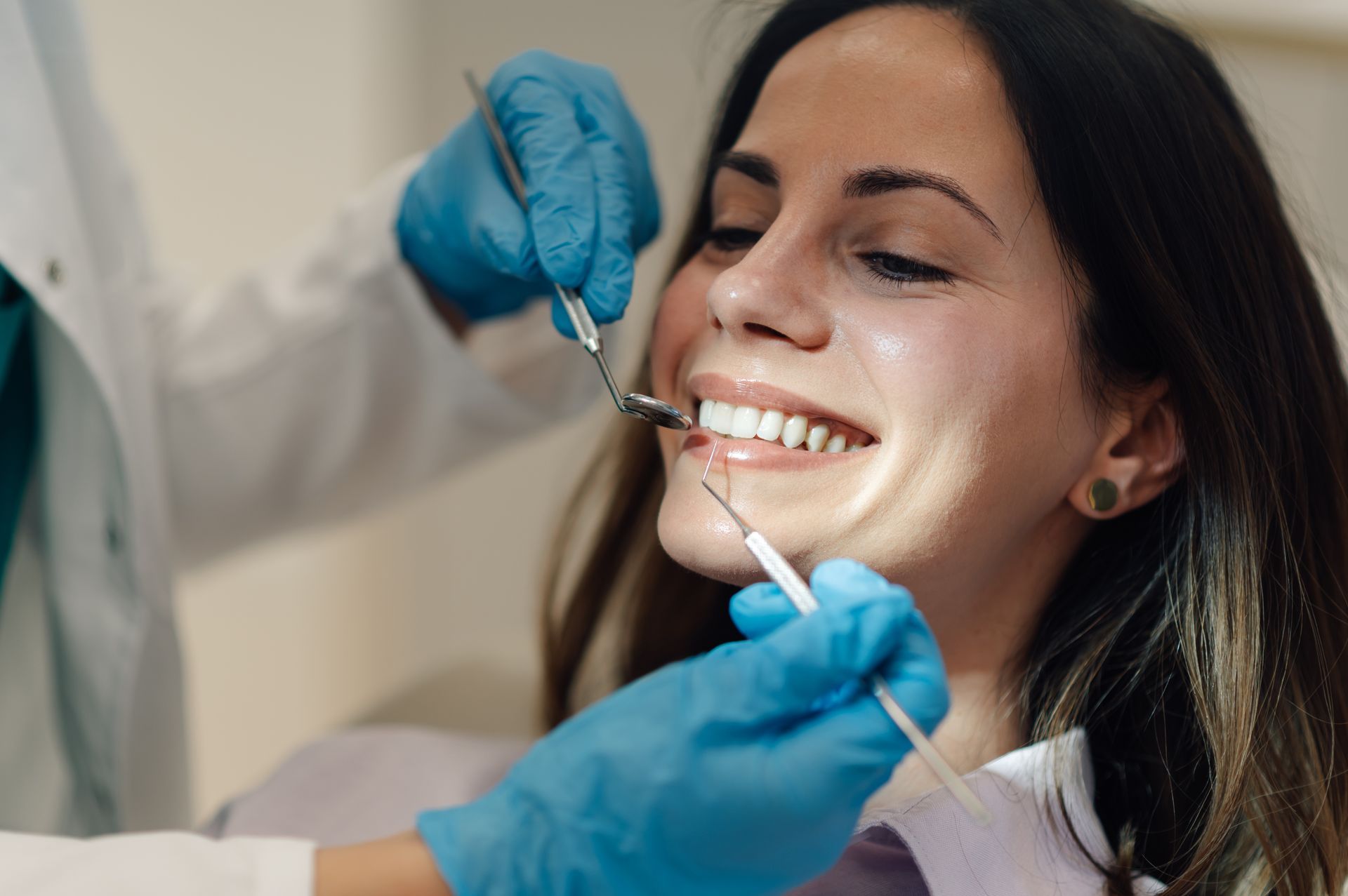 Dentist examining a smiling patient’s teeth with dental tools and blue gloves