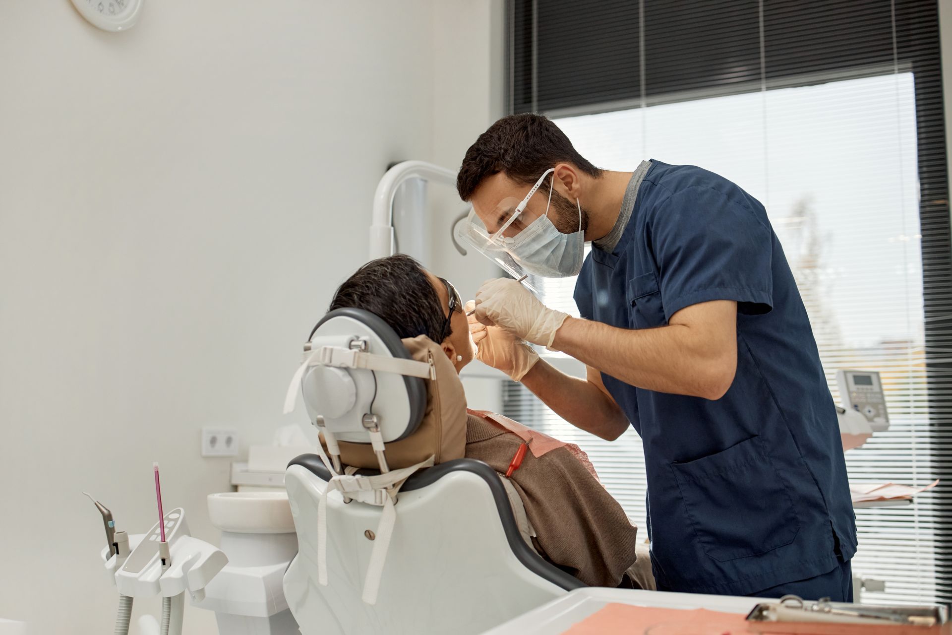 Dentist in blue scrubs examining a patient in a dental chair during a checkup