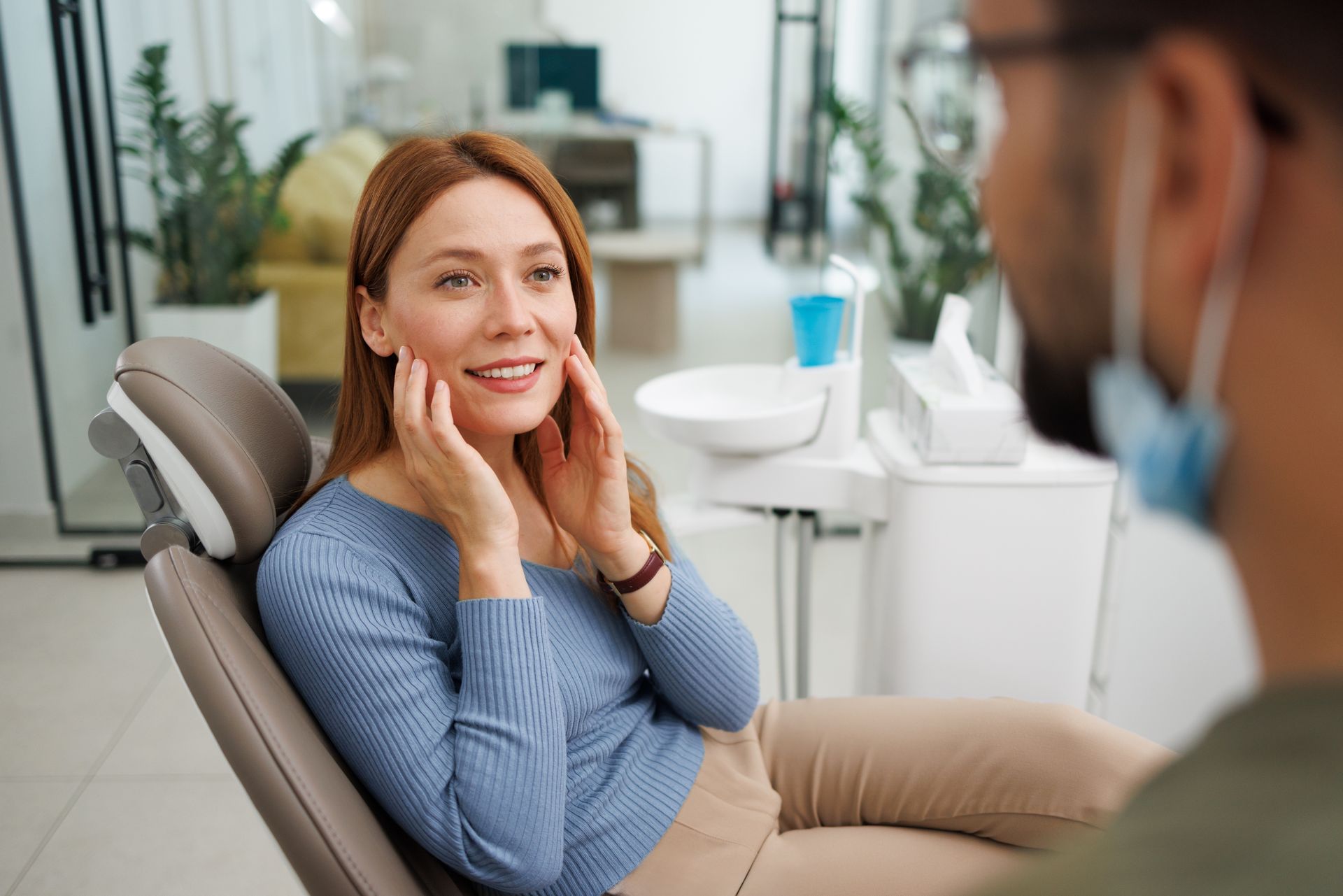 Patient smiling in a dental chair while a dentist works nearby in a bright clinic
