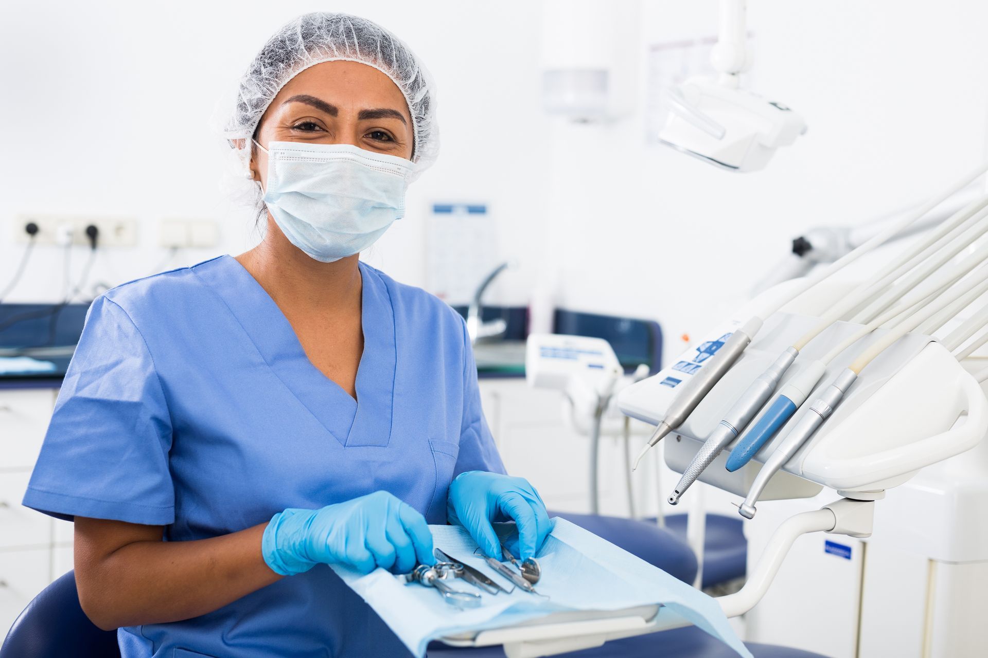 Dental professional in blue scrubs and mask working at a dental chair in a bright clinic