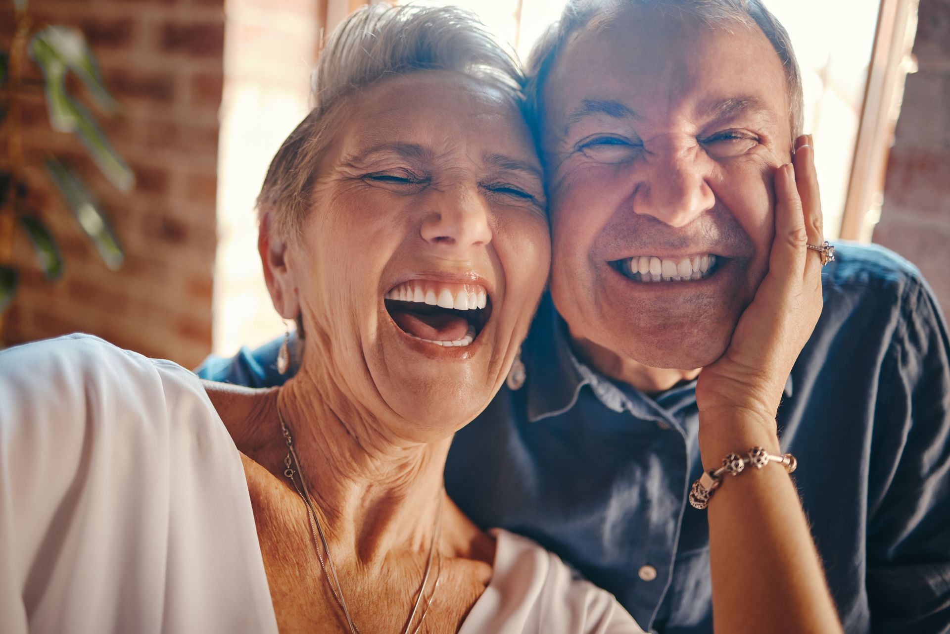 Two smiling people sitting close together, laughing in warm sunlight indoors