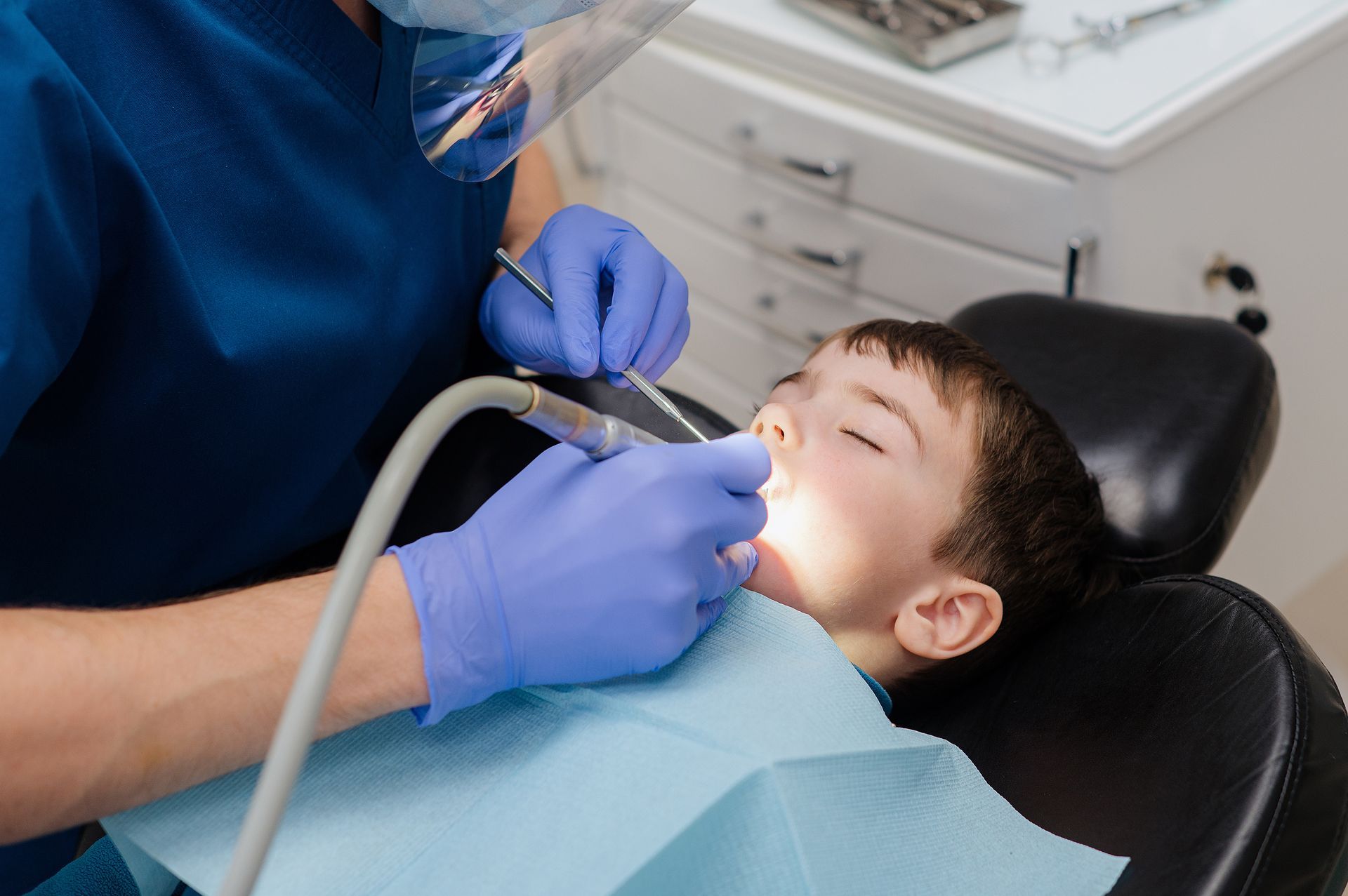 Dentist using tools to examine a child’s open mouth in a dental chair