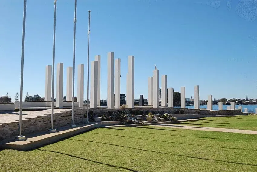 Modern sculpture of tall white pillars on a grassy lawn under a blue sky near water