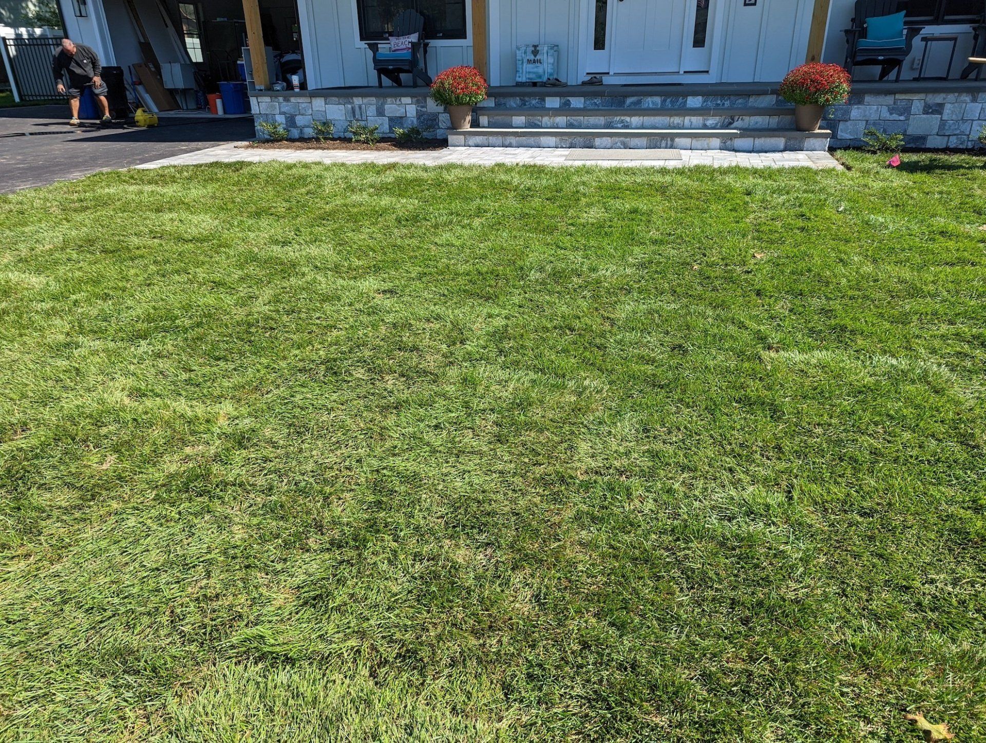 A man is standing in front of a lush green lawn in front of a house.