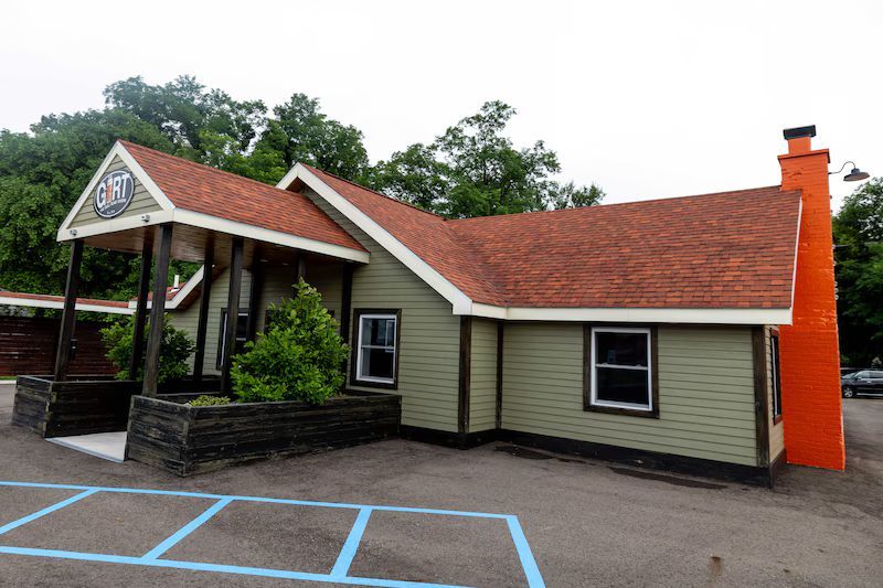 Restaurant with a green exterior and orange chimney; red roof. 