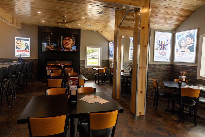 Cozy wood-paneled restaurant dining room with tables, chairs, and posters on the walls