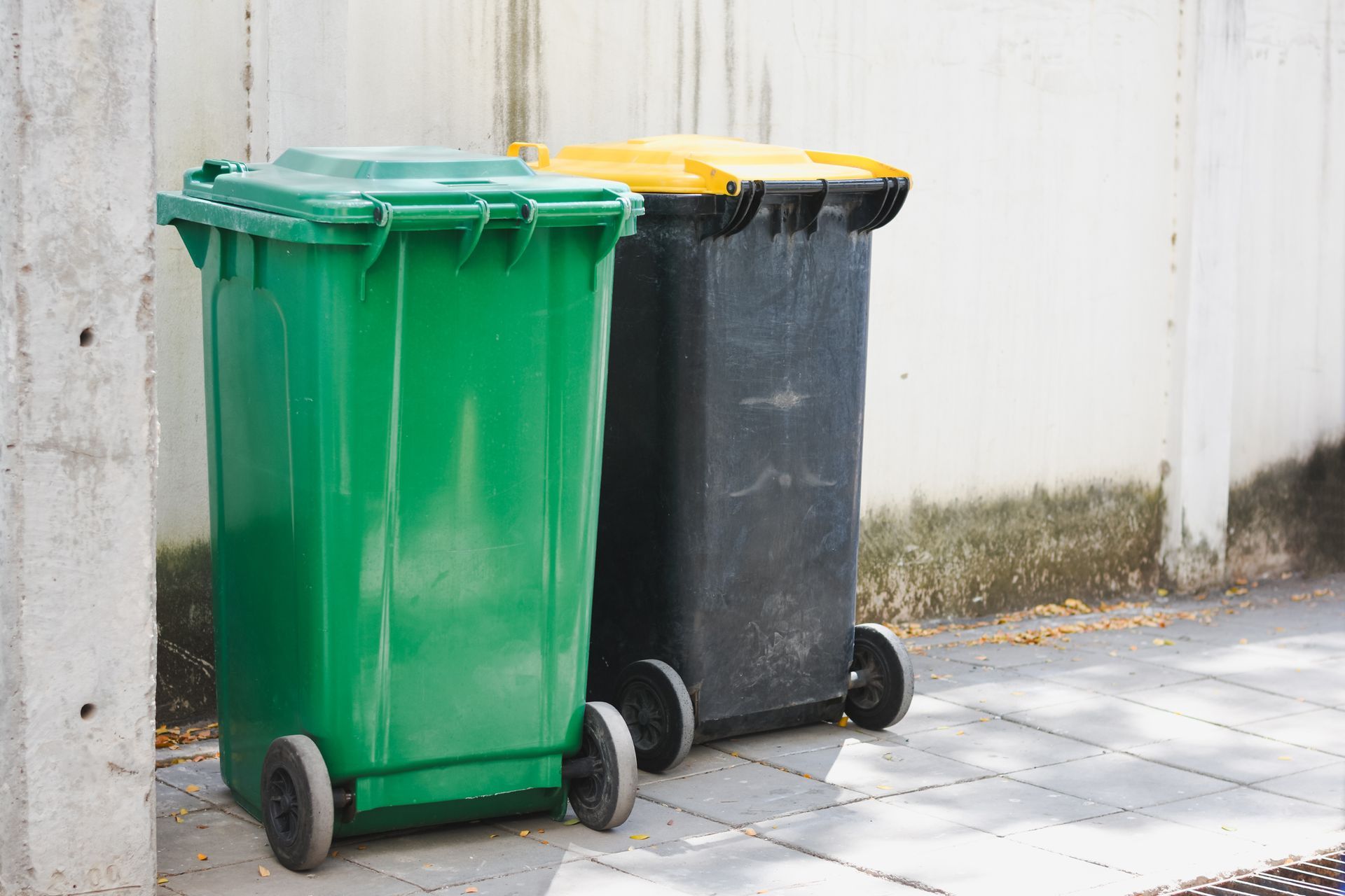 Two trash cans are sitting next to each other on the sidewalk.