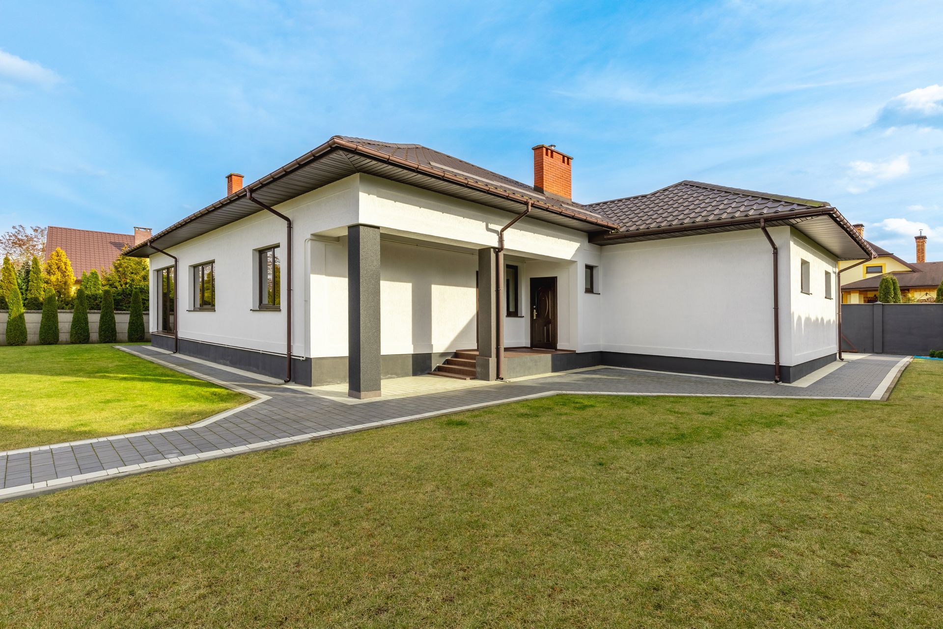 A white house with a brown roof is sitting on top of a lush green lawn.