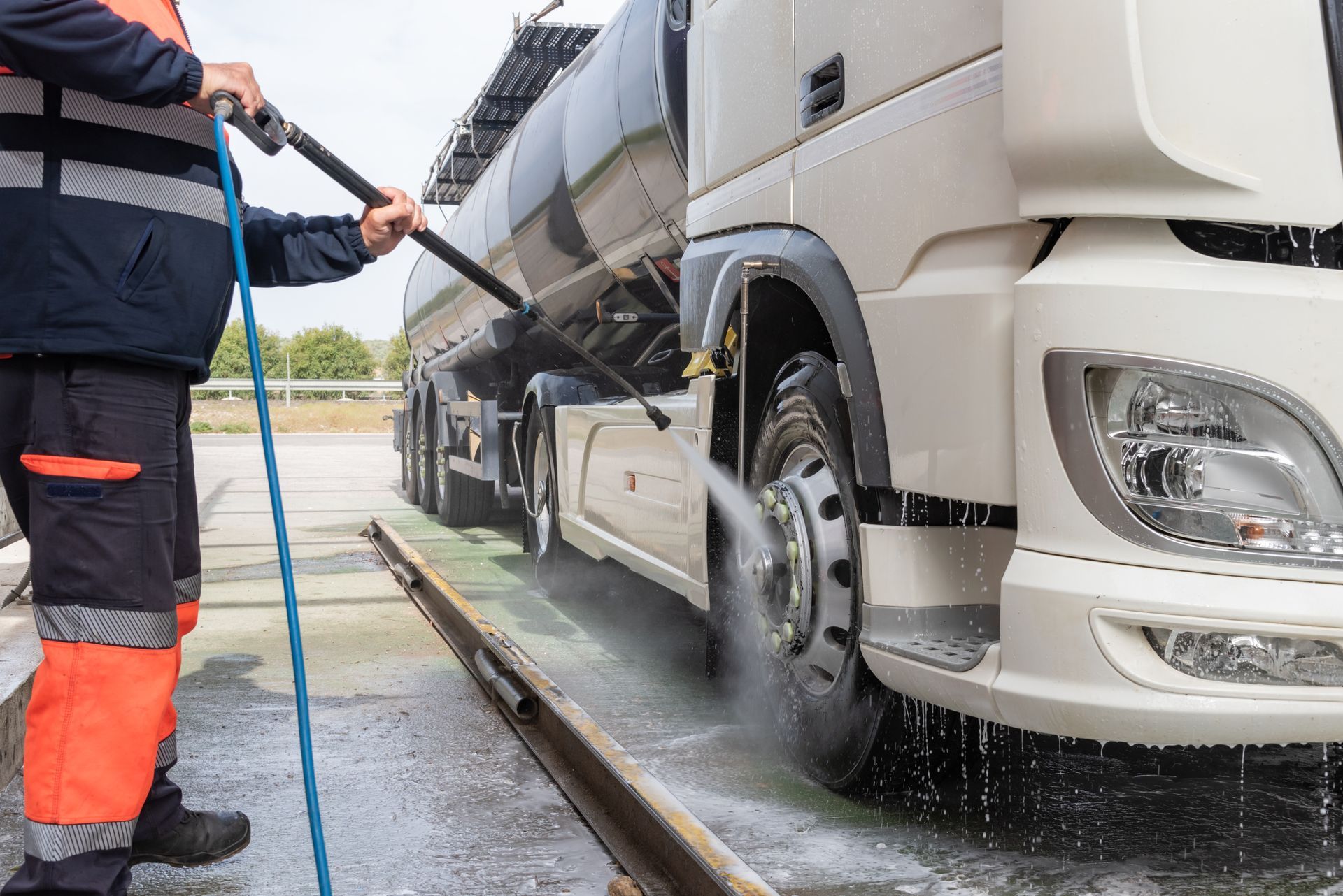 A man is washing a truck with a high pressure hose.