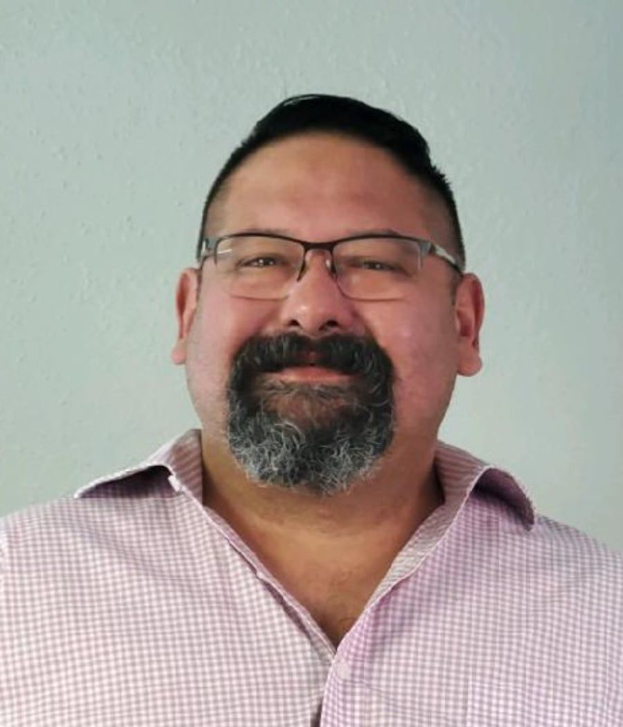 A man with a beard and glasses is wearing a pink shirt.