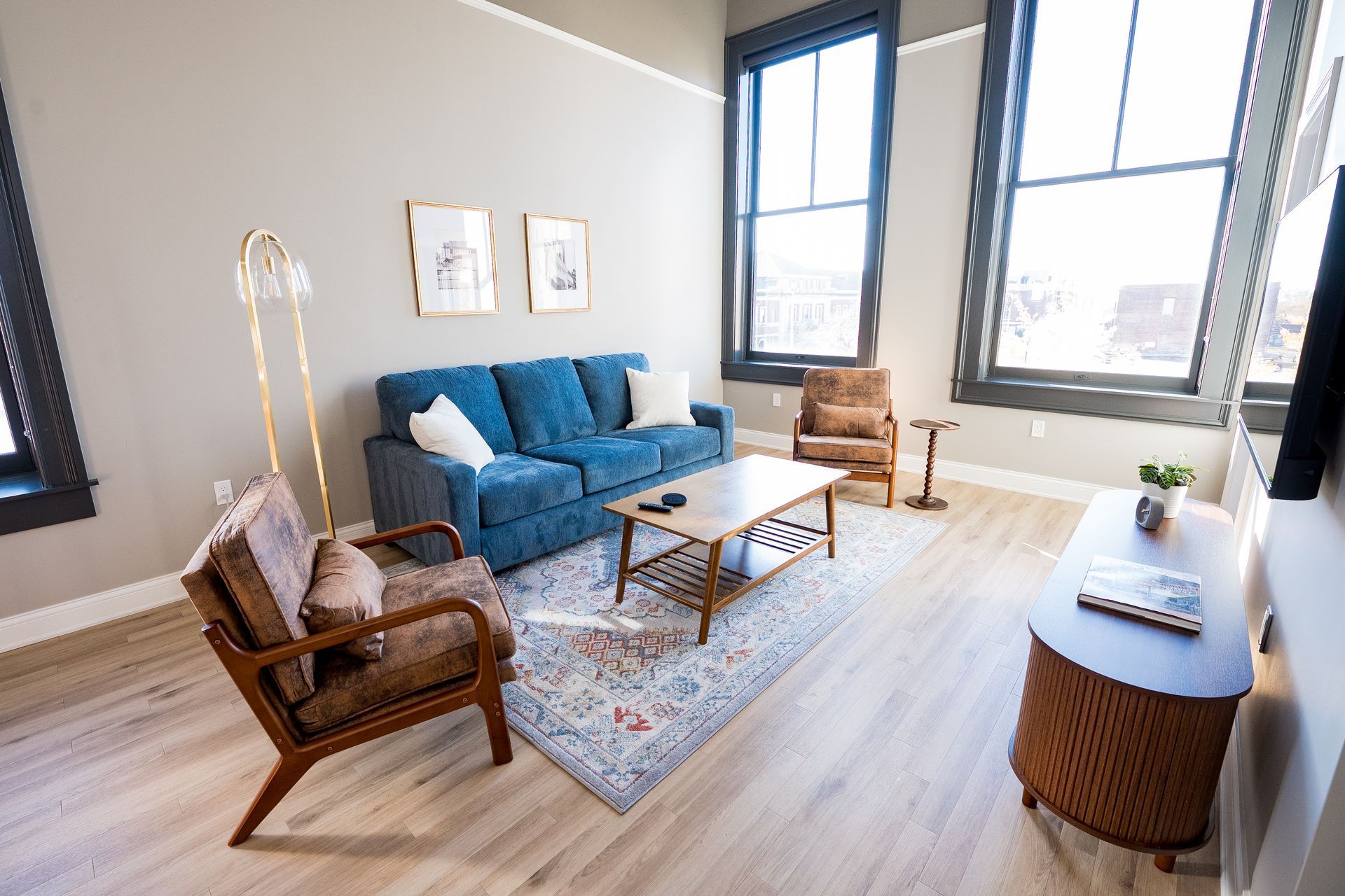 Bright living room with blue sofa, wicker chairs, rug, coffee table, and large windows